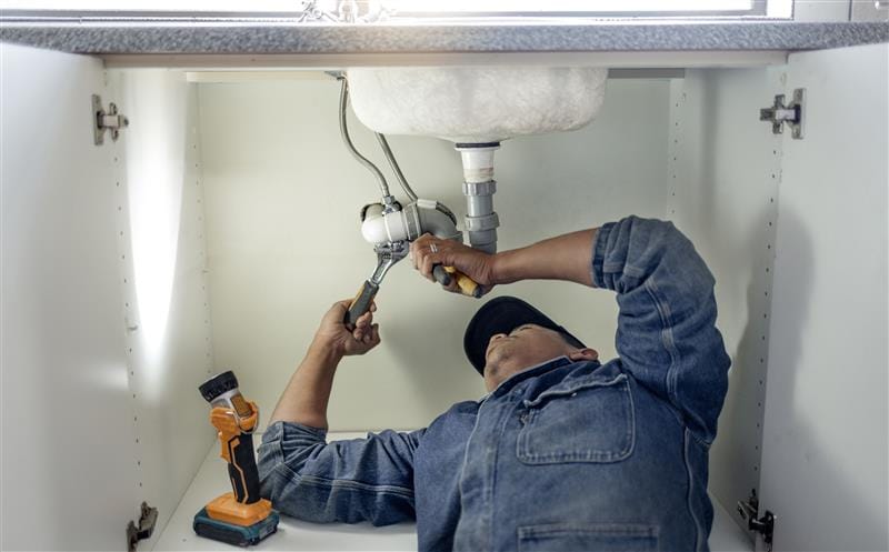 Plumber repairing pipes beneath a bathroom sink in South San Francisco
